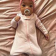 Diyonne joined the competition — help win amazing prizes! baby, infant, pacifier, pink_onesie, headband, bow, blanket, soft_texture, lying_down, cute, child, sleepwear, cozy, portrait, indoors, face, hand, footed_pajamas, young_child, newborn