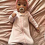 baby, infant, pacifier, pink_onesie, headband, bow, blanket, soft_texture, lying_down, cute, child, sleepwear, cozy, portrait, indoors, face, hand, footed_pajamas, young_child, newborn
