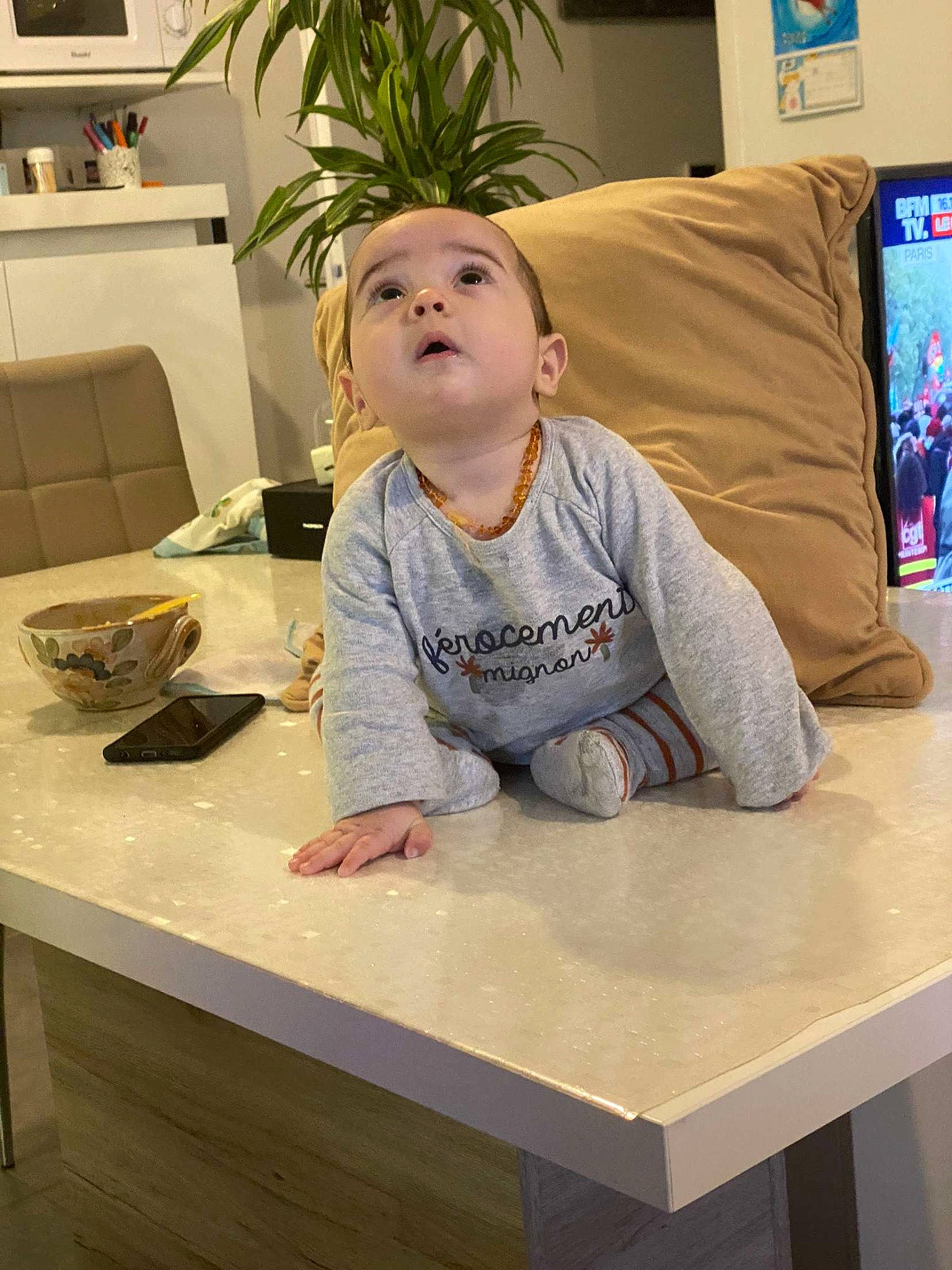 Kaïs participe au concours pour gagner de l'argent avec cette photo : baby_toddler_clothing, child, comfort, flooring, hardwood, hoodie, houseplant, kitchen_appliance, mixing_bowl, person, picture_frame, plant, room, sitting, sleeve, t_shirt, table, tableware, television, toddler