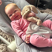 Daisy-May is registered to the contest to win money with this photo: baby, child, pink_clothing, stuffed_animal, bunny, soft_toy, baby_bouncer, cushion, smiling, happy, indoor, blanket, plush, cute, infant, relaxing, person, cozy, face, hand