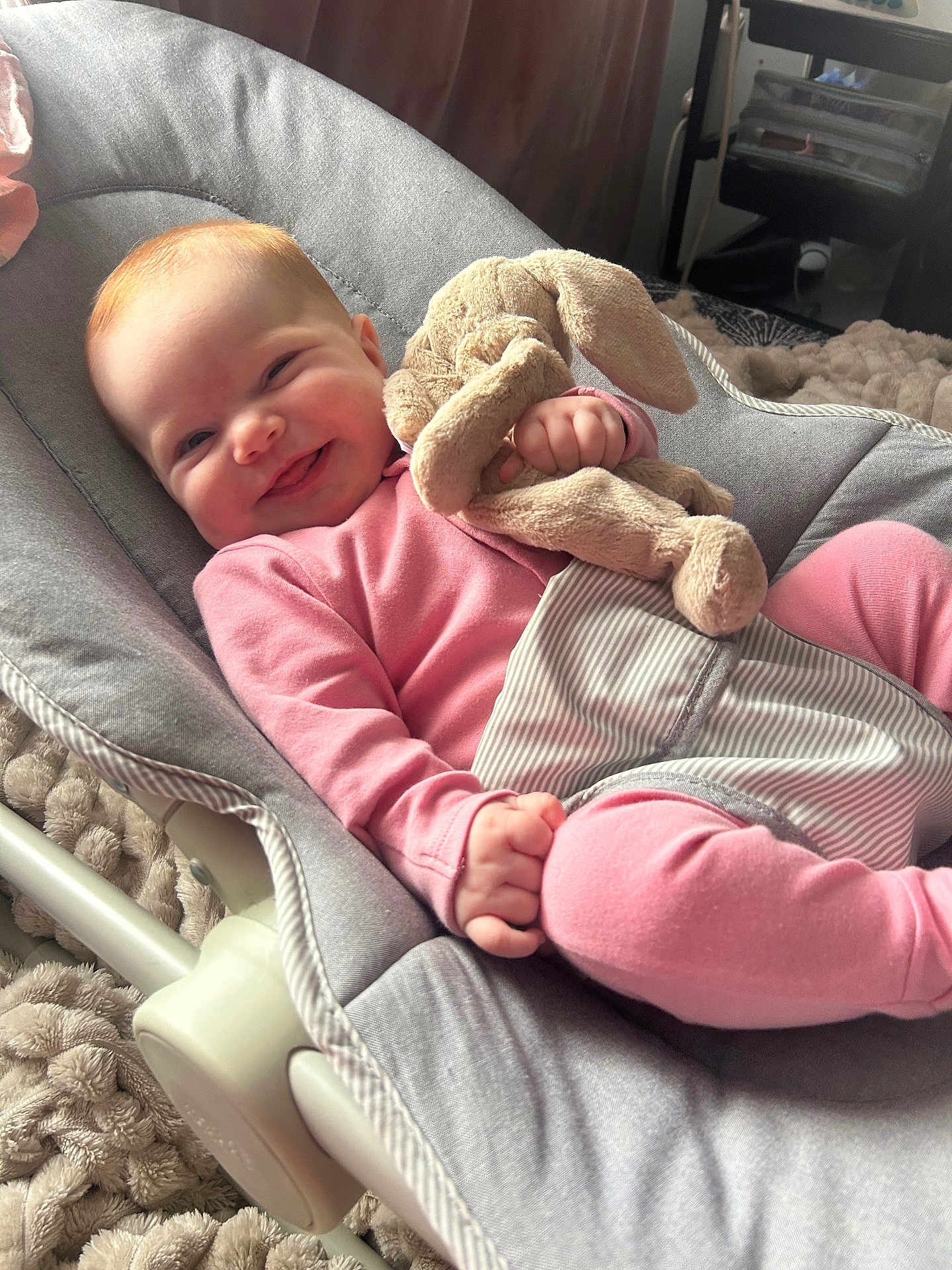 Daisy-May is registered to the contest to win money with this photo: baby, child, pink_clothing, stuffed_animal, bunny, soft_toy, baby_bouncer, cushion, smiling, happy, indoor, blanket, plush, cute, infant, relaxing, person, cozy, face, hand