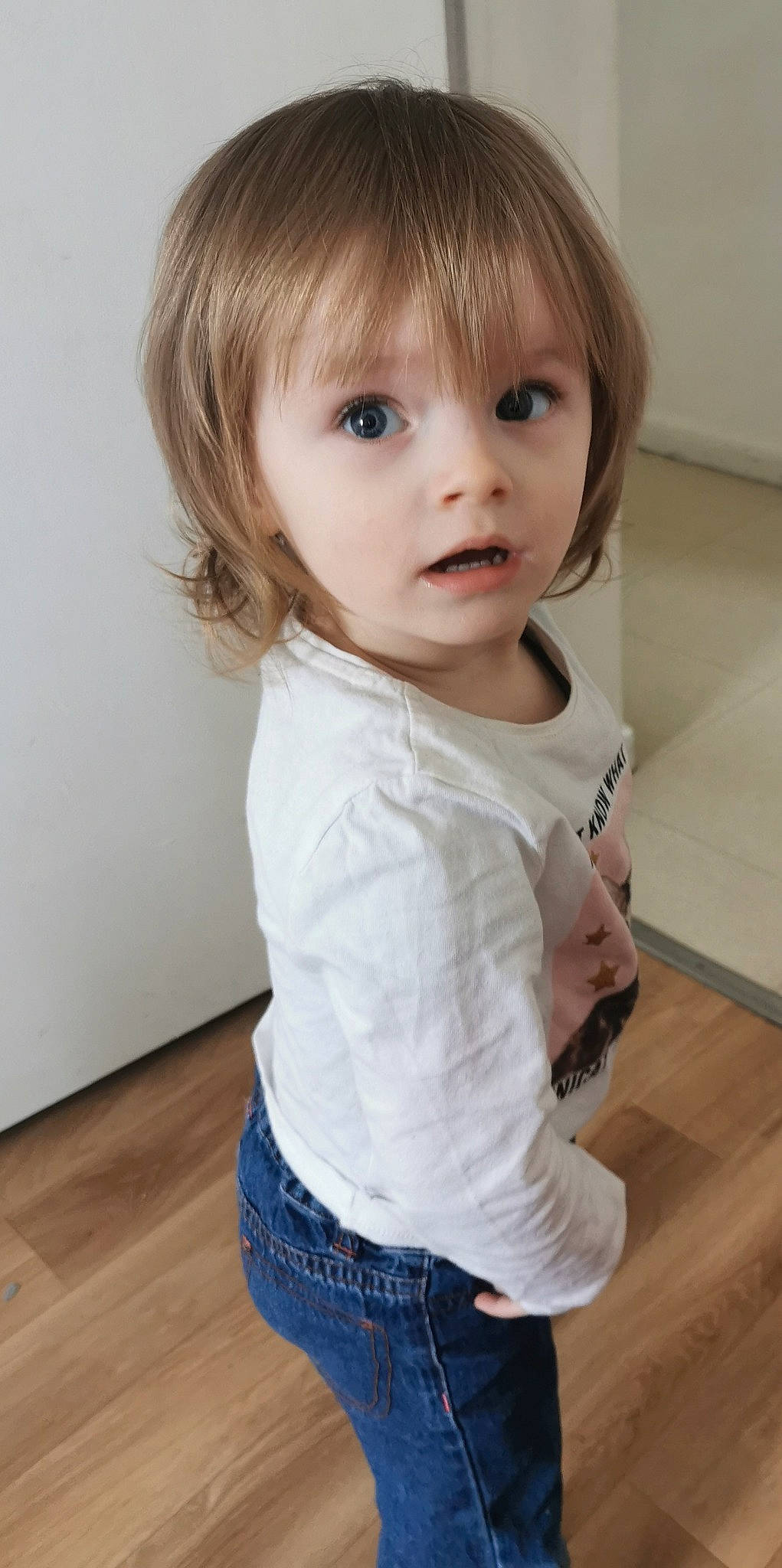 Océane a rejoint le concours — aidez-le/la à gagner de superbes lots ! baby_toddler_clothing, bangs, brown_hair, cheek, child, clothing, eye, eyelash, flooring, hardwood, lip, long_sleeved_t_shirt, neck, nose, person, sleeve, standing, surprise, toddler, waist