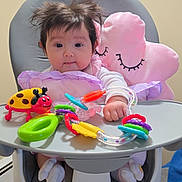 Luxana is registered to the contest to win money with this photo: baby, high_chair, toy, colorful_toy, pink_pillow, indoor, child, face, hair, socks, wooden_floor, playful, cute, infant, furniture, smiling, person, seat, happy, home