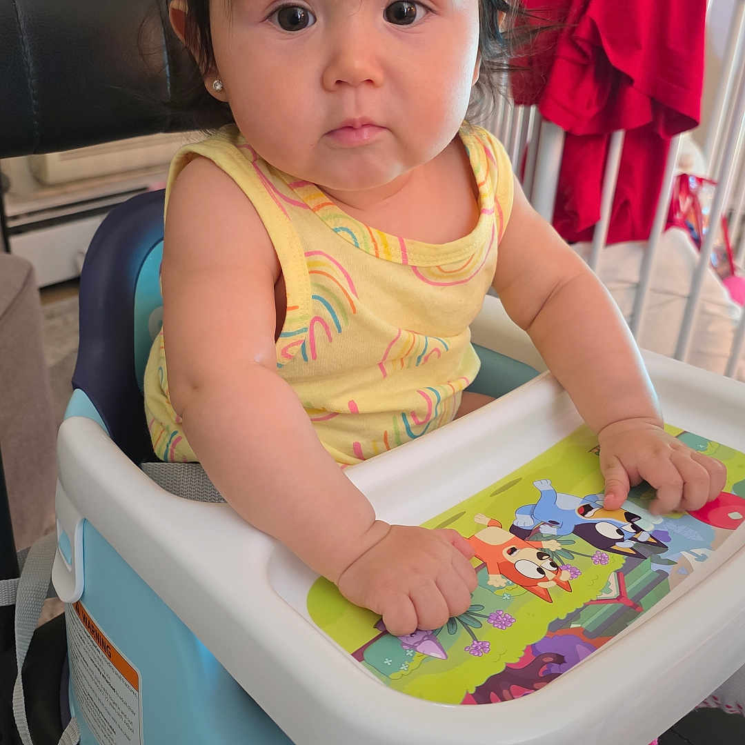 Luxana joined the competition — help win amazing prizes! baby, child, high_chair, yellow_clothing, rainbow_pattern, indoor, furniture, tray, hand, face, curious, black_hair, crib, red_clothing, carpet, earrings, window, home, person, seated