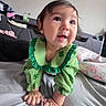 baby, child, crawling, green_clothing, clover, bed, pillow, indoor, person, cute, happy, face, hands, skin, hair, room, furniture, blanket, curious, smiling