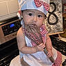 Luxana is registered to the contest to win money with this photo: baby, child, chef_hat, apron, kitchen, stove, whisk, cooking, cute, gingham, red_and_white, hat, infant, toddler, face, expression, indoor, person, sitting, foot