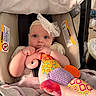 baby, child, infant, car_seat, headband, bow, blanket, plush_toy, soft_toy, hand, face, blue_eyes, clothing, indoors, cute, portrait, comfort, seated, expression, infant_toy