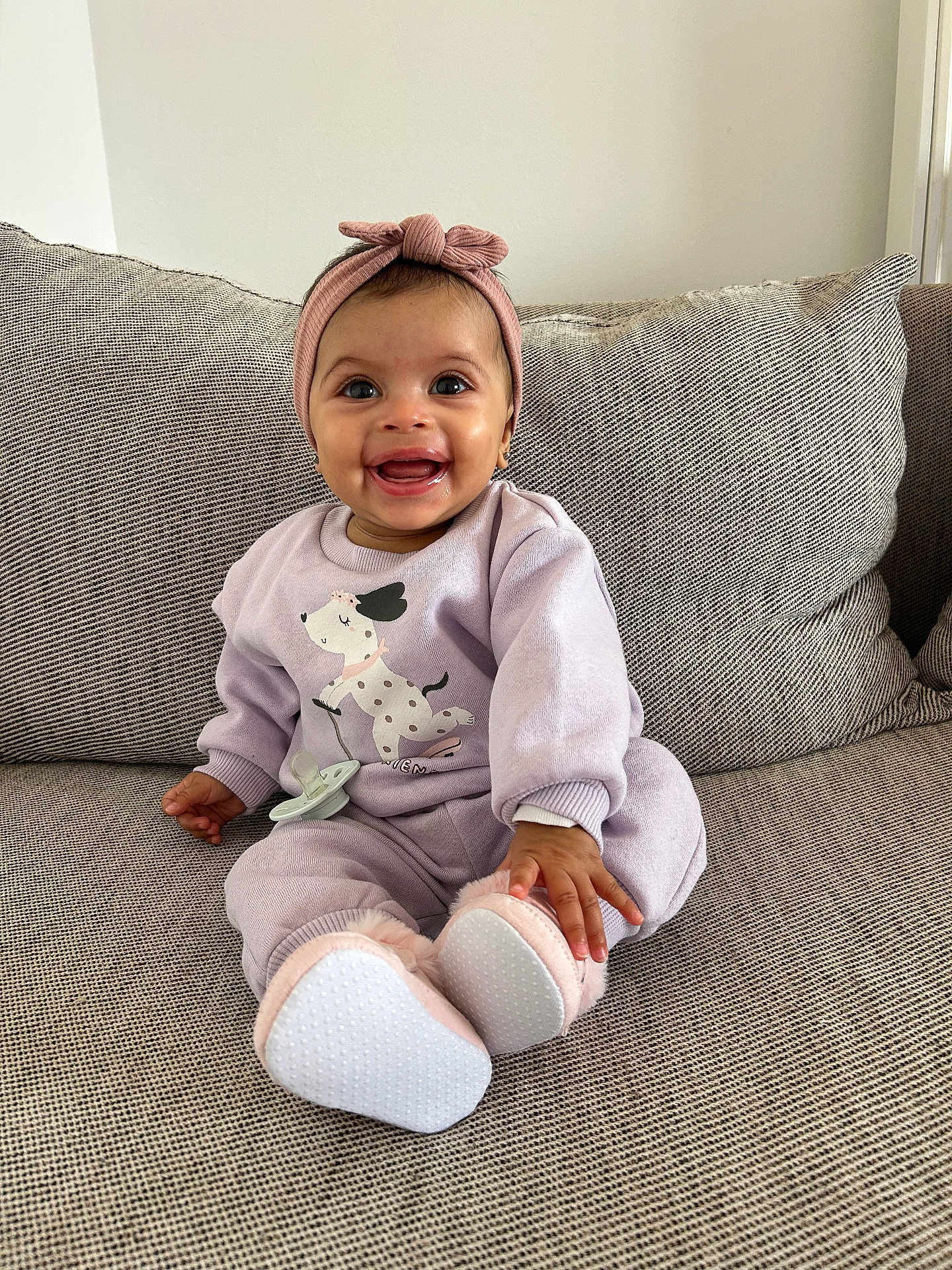 Maelya participe au concours pour gagner de l'argent avec cette photo : baby, infant, smiling, headband, onesie, pacifier, slippers, couch, pillow, sitting, portrait, cute, indoor, homedecor, child, happy, eyes, hands, feet, cozy
