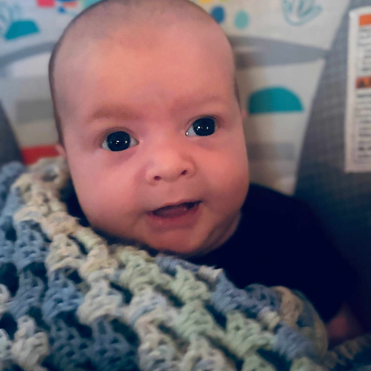 Braxton is registered to the contest to win money with this photo: baby, infant, face, blanket, knitted_blanket, smile, happy, closeup, cute, child, portrait, indoors, young_child, colorful_background, eyes, head, skin, person, warm, cozy