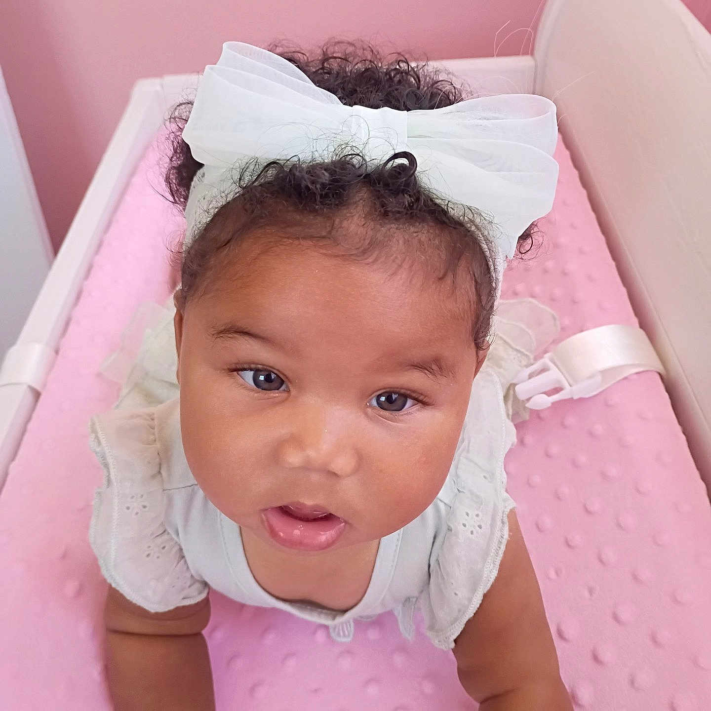 Micha joined the competition — help win amazing prizes! baby, infant, child, portrait, smiling, wide_eyed, white_bow, curly_hair, pink_crib, pink_blanket, nursery, lying_down, sitting, onesie, white_clothing, headband, close_up, face, indoors, adorable