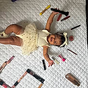 Ayleen joined the competition — help win amazing prizes! baby, child, infant, smiling, lying_down, white_bedspread, makeup_products, lipstick, brush, cosmetics, headband, dress, tutu, happy, cute, arm_up, legs_bent, skin, beauty, indoor