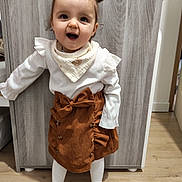 Ava a rejoint le concours — aidez-le/la à gagner de superbes lots ! child, toddler, smiling, mouth_open, pigtails, hair_bow, bib, white_top, corduroy_skirt, bow, tights, socks, wood_floor, wardrobe, indoor, portrait, standing, happy, cute, playful