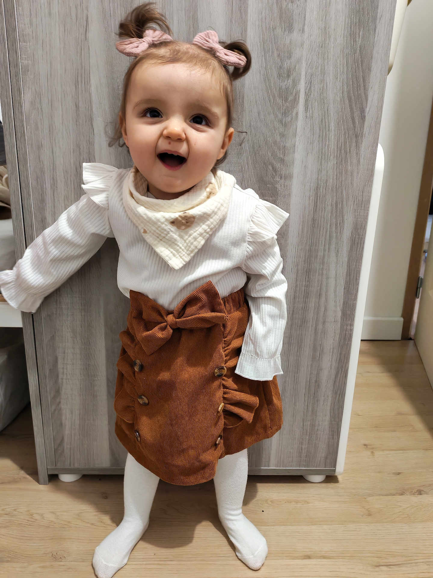 Ava a rejoint le concours — aidez-le/la à gagner de superbes lots ! child, toddler, smiling, mouth_open, pigtails, hair_bow, bib, white_top, corduroy_skirt, bow, tights, socks, wood_floor, wardrobe, indoor, portrait, standing, happy, cute, playful