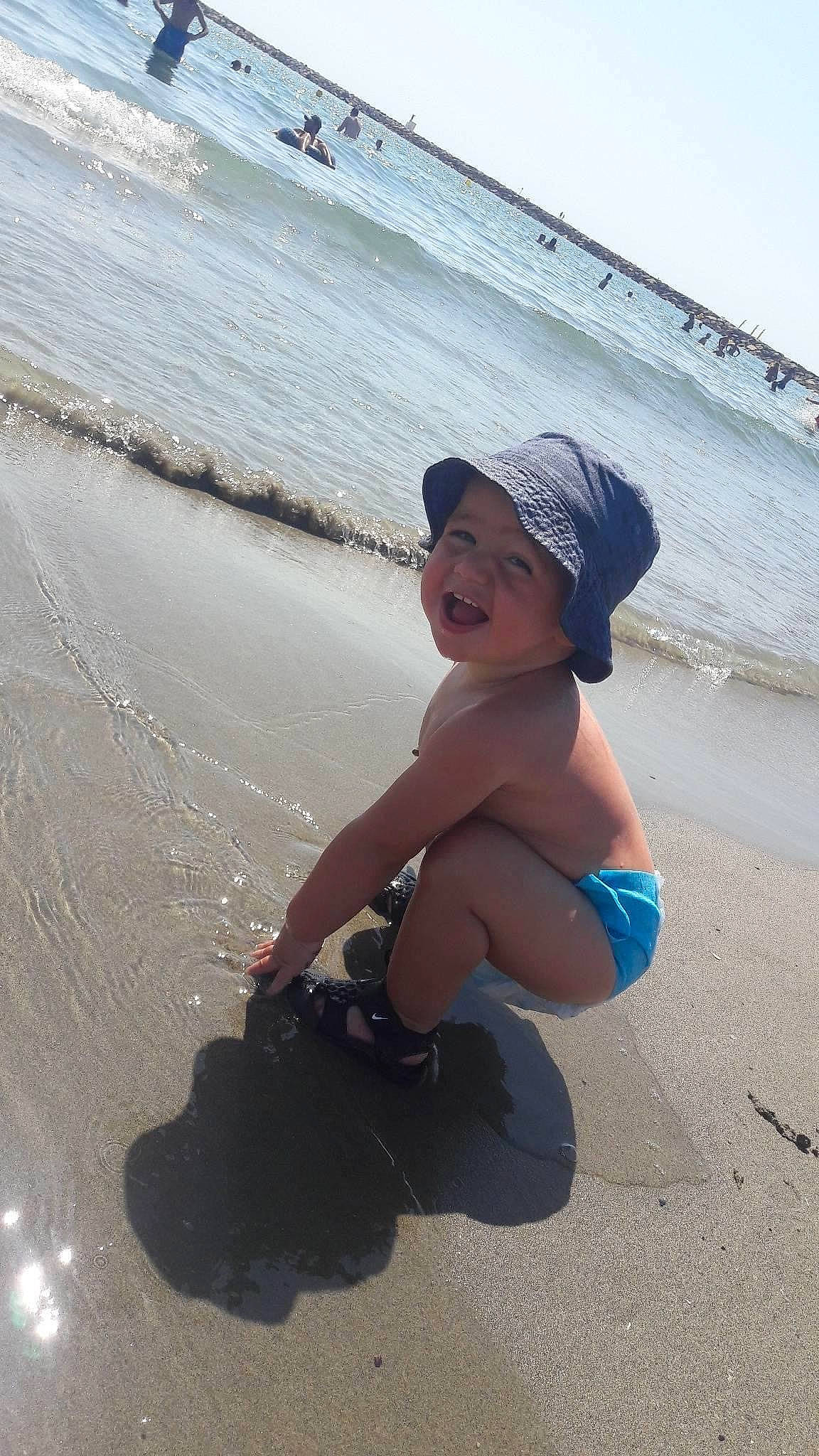 Leny participe au concours pour gagner de l'argent avec cette photo : beach, body_of_water, fun, happy, hat, headwear, leisure, people_in_nature, people_on_beach, person, personal_protective_equipment, recreation, sand, shorts, sky, smile, sun_hat, thigh, toddler, travel