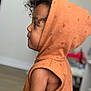 child, toddler, hood, orange_clothing, curly_hair, profile, indoor, sleeveless, cute, young_child, side_view, soft_lighting, skin, face, person, clothing, portrait, childhood, expression, casual