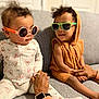 Rylan is registered to the contest to win money with this photo: toddler, baby, sunglasses, child, couch, indoor, clothing, hand_holding, person, cute, fashion, smile, curly_hair, sitting, cozy, watch, adult_hand, orange, gray, playful