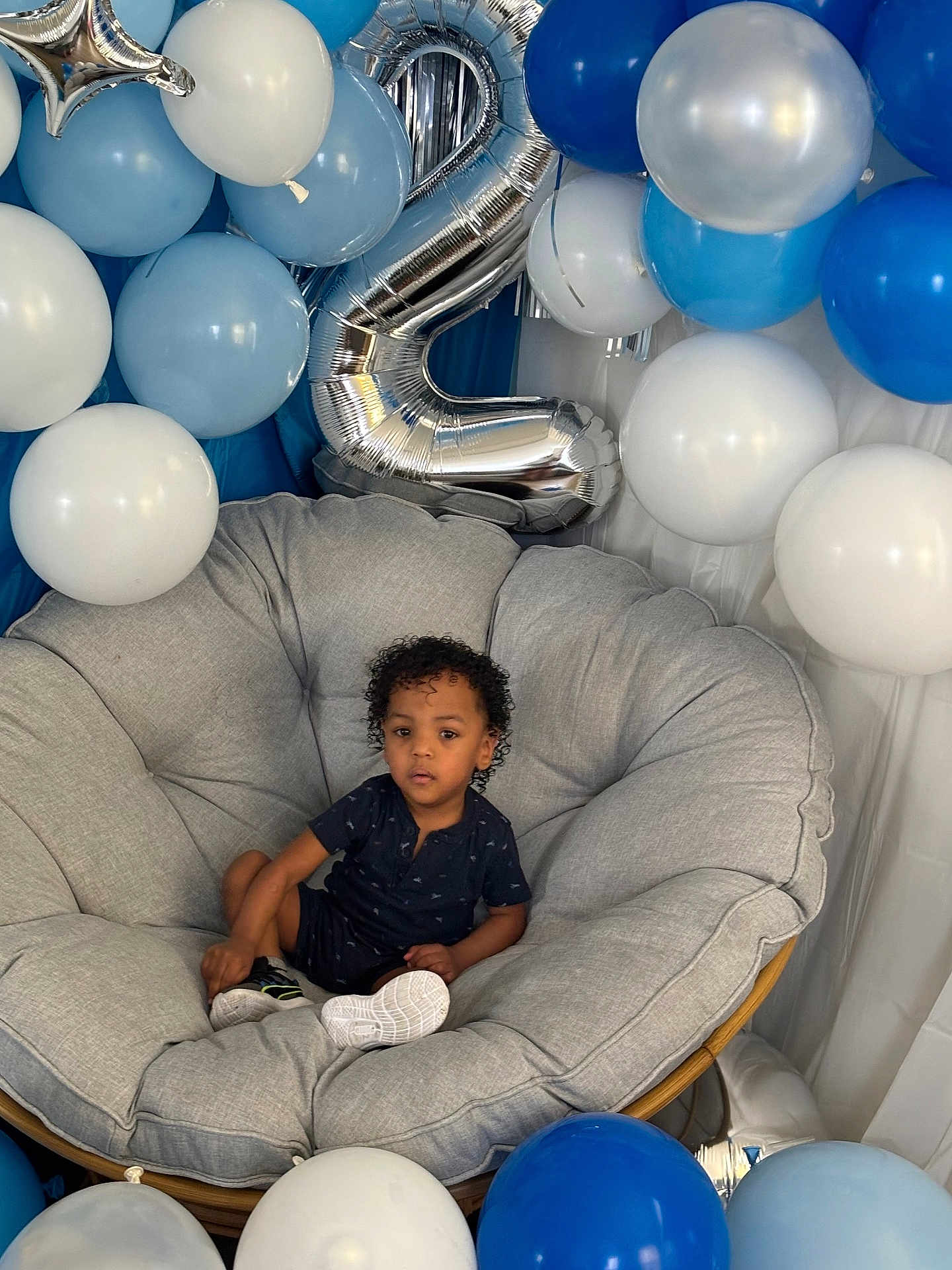 Rylan joined the competition — help win amazing prizes! child, balloons, birthday, chair, cushion, blue, white, silver, number_two, curly_hair, shoes, celebration, indoor, person, smiling, comfortable, party, decorations, happy, casual_clothing