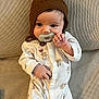 baby, infant, pacifier, brown_hat, onesie, teddy_bear_print, couch, fabric_texture, lying_down, cute, child, small_hand, face, indoors, cozy, comfortable, young_child, sleepwear, knit_hat, portrait