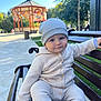 baby, child, bench, park, outdoor, knitwear, beanie, cute, smiling, person, daylight, gazebo, trees, greenery, public_space, wood, sitting, face, blue_eyes, casual