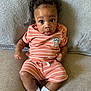 baby, infant, child, couch, clothing, striped_outfit, socks, face, curly_hair, expression, indoor, portrait, cute, small_hands, seated, soft_texture, cartoon_patch, orange, white, cozy