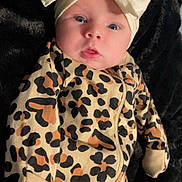 Octavia is registered to the contest to win money with this photo: baby, infant, headband, bow, leopard_print, onesie, clothing, face, eyes, mouth, blanket, black_background, cute, child, portrait, lying_down, soft_texture, newborn, warm, cozy