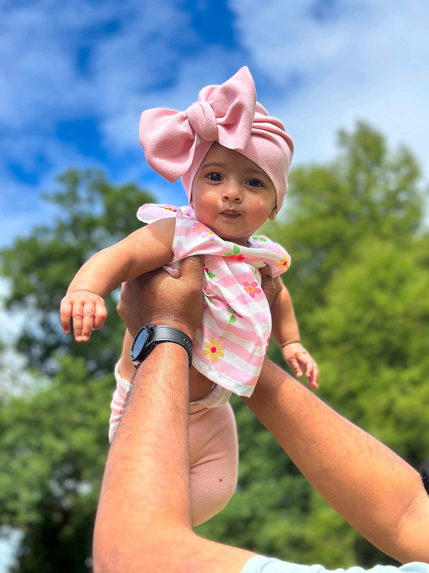 Amelia joined the competition — help win amazing prizes! baby, child, pink_bow, headwrap, floral_top, hands, adult, outdoor, blue_sky, greenery, watch, portrait, cute, smile, person, nature, daylight, holding, happy, infant