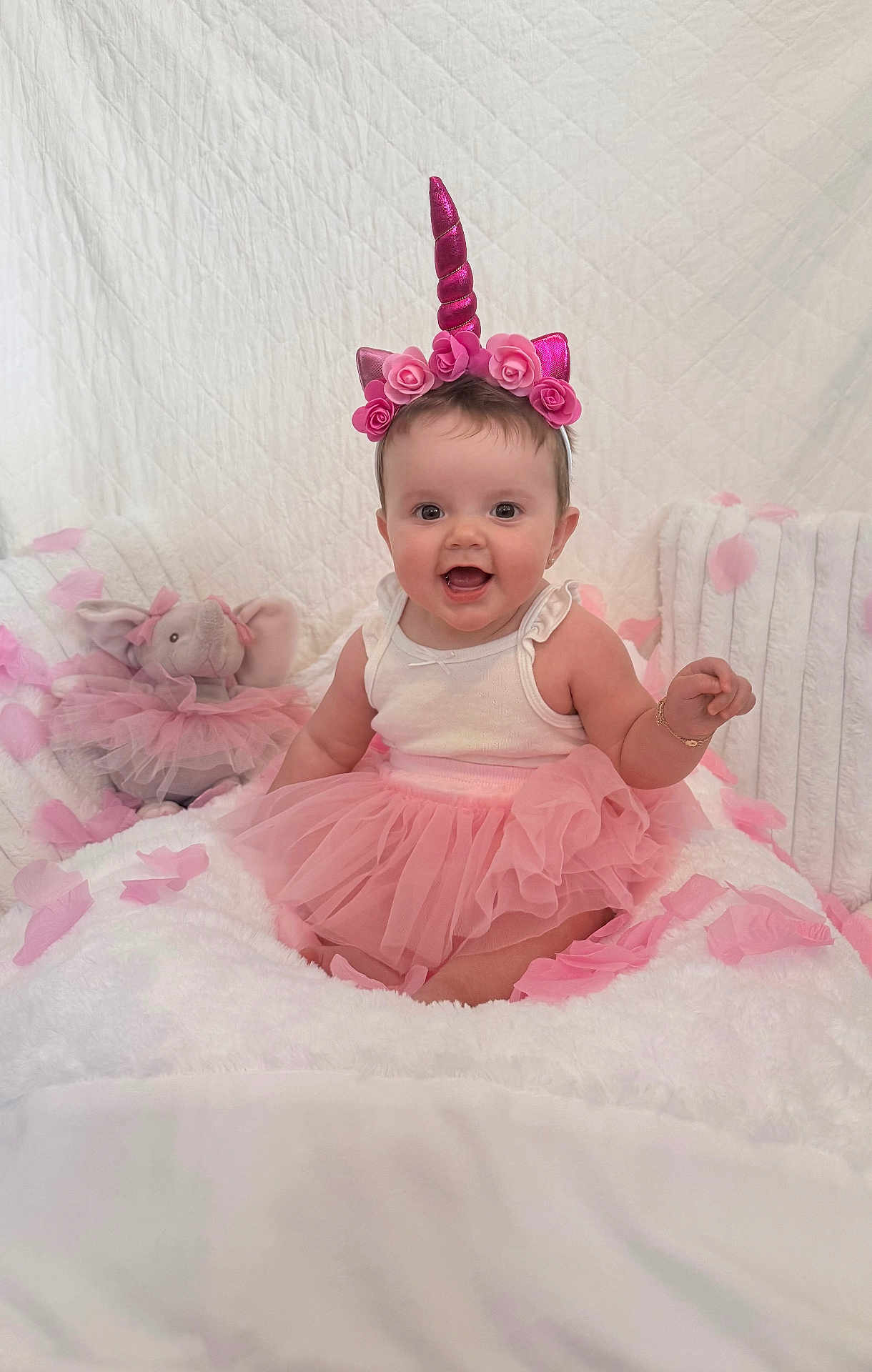 Amber joined the competition — help win amazing prizes! baby, child, unicorn_headband, pink_tutu, smiling, sitting, stuffed_animal, elephant_toy, fluffy_blanket, pink_petals, white_background, cute, happy, portrait, indoor, adorable, infant, headband, dress, playful