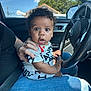 Oliver is registered to the contest to win money with this photo: baby, child, car, steering_wheel, curly_hair, person, hand, clothing, seatbelt, window, blue_sky, tree, jeans, shirt, indoor, vehicle_interior, portrait, surprised, sitting, adult_hand