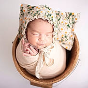 Melissa a rejoint le concours — aidez-le/la à gagner de superbes lots ! newborn, baby, infant, swaddle, bonnet, wooden_bucket, floral_pattern, pillow, sleeping, peaceful, portrait, closeup, soft_lighting, cute, child, headwear, hands, resting, studio_photo, neutral_background