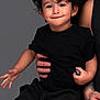 toddler, child, curly_hair, black_clothing, smiling, playful, portrait, studio, adult_hand, holding, neutral_background, happy, cute, person, indoors, short_sleeves, casual_wear, young_child, human, expression
