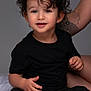 Gabriel a rejoint le concours — aidez-le/la à gagner de superbes lots ! toddler, child, curly_hair, black_clothing, sitting, smiling, tattoo, arm, bed, white_bed, portrait, cute, indoor, happy, person, young_child, casual, studio_lighting, closeup, human