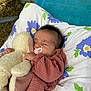 baby, sleeping, teddy_bear, pacifier, blanket, pillow, floral_pattern, outdoor, grass, child, infant, cute, peaceful, resting, cozy, soft_toy, clothing, nature, portrait, relaxation