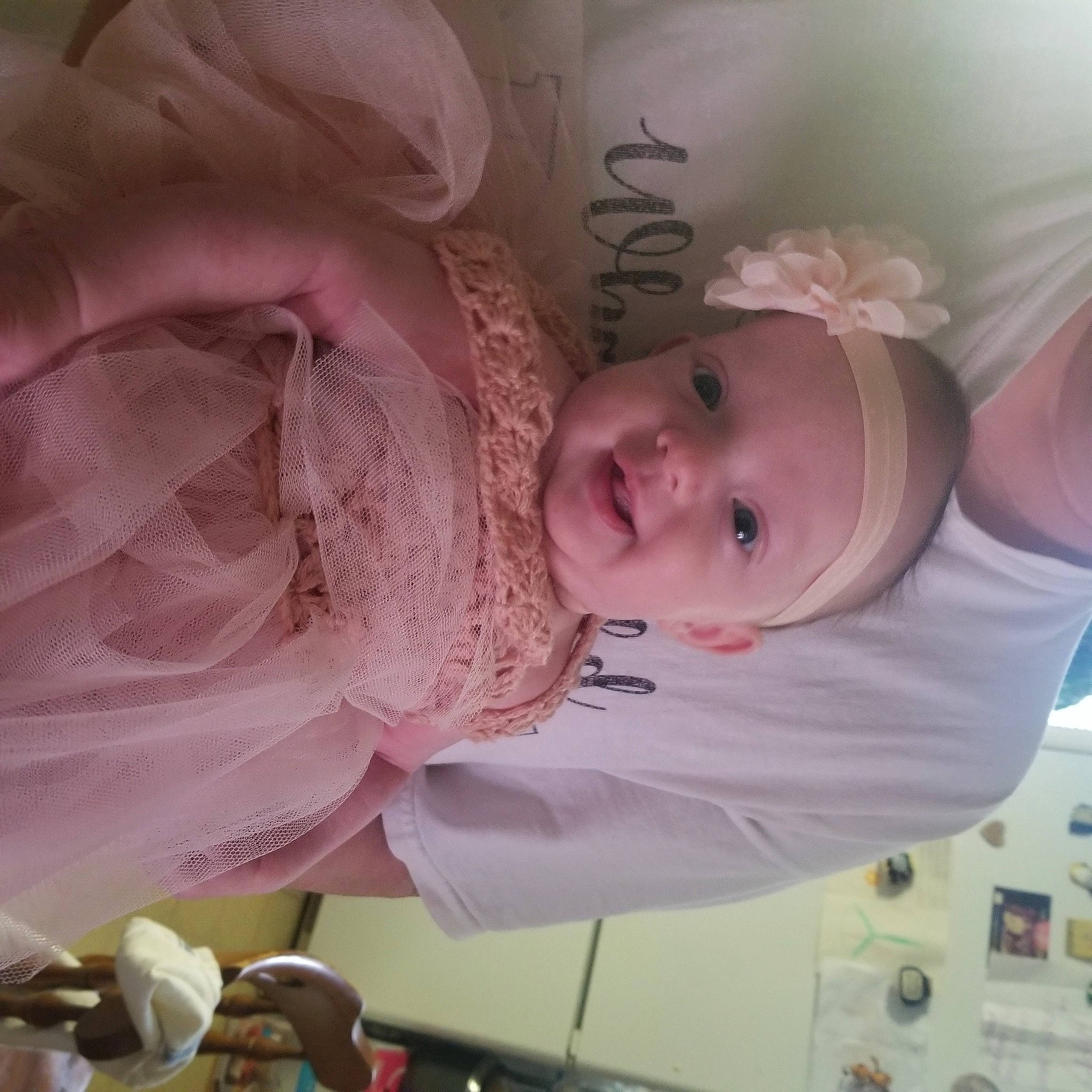 Fianna is registered to the contest to win money with this photo: baby, baby_products, baby_toddler_clothing, child, dress, embellishment, event, eyebrow, finger, hair_accessory, happy, iris, peach, person, pink, room, rose, skin, smile, textile
