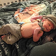 Colter is registered to the contest to win money with this photo: baby, newborn, infant, hat, bow_tie, suspenders, plaid_pants, blanket, bed, lying_down, smile, face, belly_button, cozy, indoors, portrait, props, cute, patterned_clothing, skin