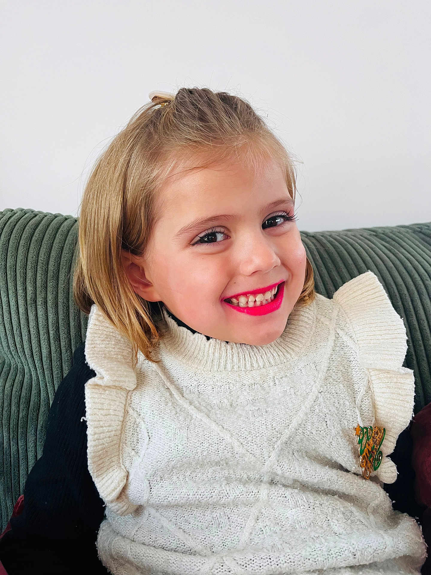 Lyla participe au concours pour gagner de l'argent avec cette photo : child, girl, smiling, lipstick, white_sweater, knitted, ruffles, brooch, green_couch, indoor, portrait, happy, young, casual_clothing, hairclip, seated, cozy, cute, fashion, face