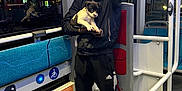 Kalash participe au concours pour gagner de l'argent avec cette photo : bus, casual_clothing, dog, floor, handrail, holding, hooded_jacket, interior, lights, night, person, pet, puppy, reflection, seating, signage, sneakers, standing, transportation, window