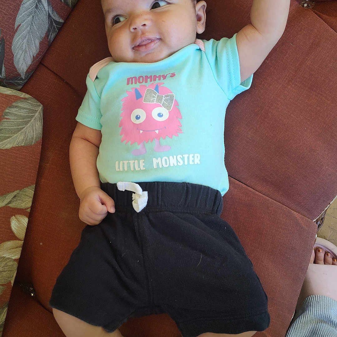 Rosealynn joined the competition — help win amazing prizes! baby, child, clothing, couch, cute, face, foot, furniture, graphic, hand, happy, indoor, infant, person, playful, relaxing, shorts, smiling, text, tshirt