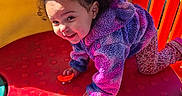 Janiyah joined the competition — help win amazing prizes! toddler, child, curly_hair, purple_jacket, playground, play_equipment, crawling, smiling, outdoor, red_surface, yellow_wall, blue_circle, happy, cute, young_child, fun, daylight, casual_clothing, playtime, person