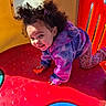 blue_circle, casual_clothing, child, crawling, curly_hair, cute, daylight, fun, happy, outdoor, person, play_equipment, playground, playtime, purple_jacket, red_surface, smiling, toddler, yellow_wall, young_child