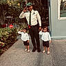 building, cap, child, greenery, happy, nature, outdoor, pacifier, person, plants, salute, sandals, security_guard, shorts, sidewalk, smile, tie, toddler, uniform, window