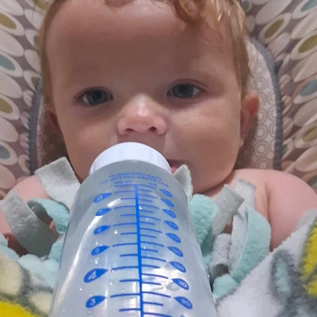 Vyxin is registered to the contest to win money with this photo: baby, bottle, blanket, curly_hair, cushion, face, feeding, infant, inside, lying_down, person, portrait, resting, soft_texture, toddler, water_bottle, young_child, blue, white, patterned_background