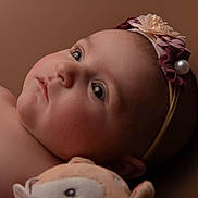 Rose a rejoint le concours — aidez-le/la à gagner de superbes lots ! baby, infant, headband, flower, pearl, soft_toy, closeup, portrait, skin, face, blue_eyes, cheeks, nose, ear, child, laying_down, warm_tones, background, cute, expression