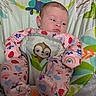 baby, infant, child, portrait, sitting, bouncer, blanket, pajamas, pink_clothing, strawberry_pattern, rainbow_pattern, sloth_toy, elephant_design, colorful, indoors, baby_gear, face, eyes_open, serious_expression, textile