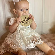 Aaliyah Rosalina joined the competition — help win amazing prizes! baby, child, twelve_months, lace_dress, headband, bow, wooden_sign, chewing, sitting, blanket, soft_texture, cute, infant, portrait, indoor, light_skin, happy, curious, one_year_old, feet