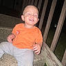 toddler, child, sitting, stairs, outdoor, night, smiling, orange_shirt, gray_pants, concrete, wooden_railing, grass, happy, casual_clothing, person, young_child, steps, playful, small, cute