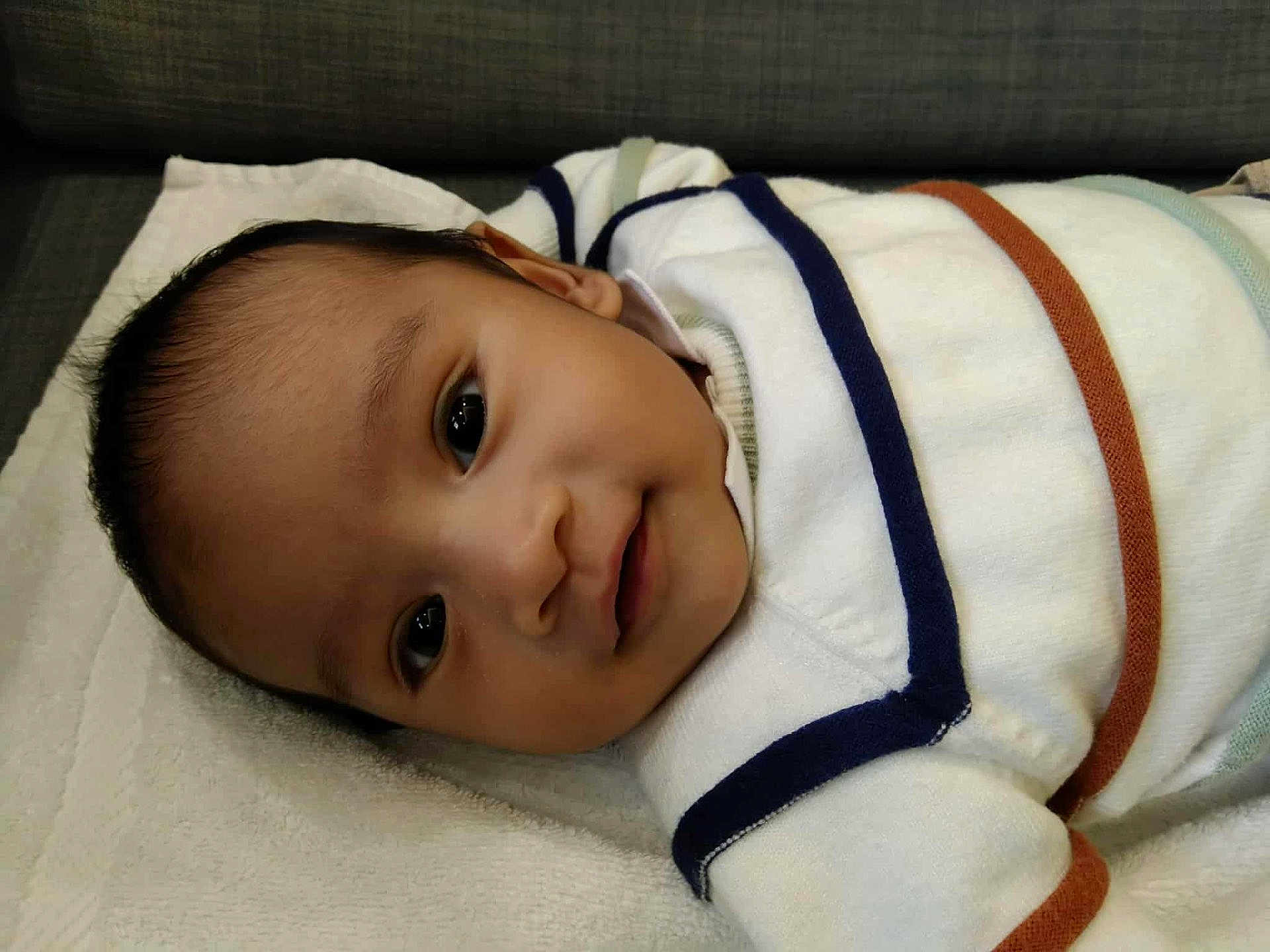 Alexandre participe au concours pour gagner de l'argent avec cette photo : baby, infant, smile, face, eyes, clothing, striped_sweater, towel, lying_down, cute, skin, child, portrait, indoors, head, young, person, warm, comfortable, closeup