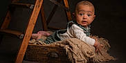 Ezra is registered to the contest to win money with this photo: baby, infant, wooden_ladder, burlap_cloth, wooden_drawer, curious, wide_eyes, studio, dim_lighting, rustic, brown, cozy_clothing, child, portrait, cute, indoors, floor, expression, small_hands, surprised
