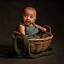 Ezra joined the competition — help win amazing prizes! baby, child, basket, overalls, blanket, curious, indoor, portrait, expression, wicker, green_clothing, infant, cute, studio_lighting, young_child, sitting, face, head, hands, dark_background