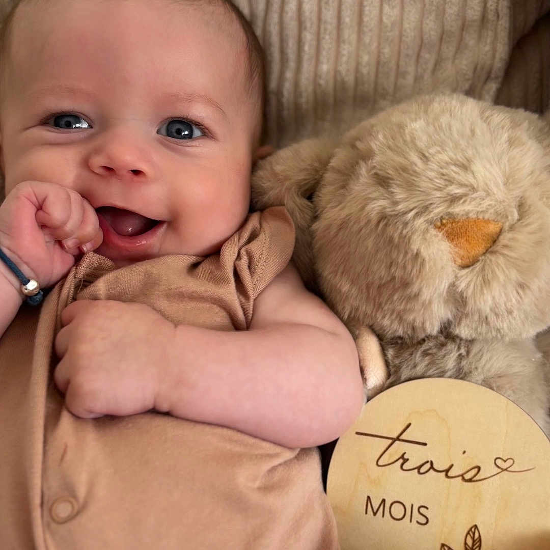 Gabriel a rejoint le concours — aidez-le/la à gagner de superbes lots ! baby, bracelet, brown_clothing, child, closeup, couch, cushion, cute, face, furniture, hand, happy, indoor, infant, milestone, plush_toy, portrait, skin, smiling, wooden_plaque