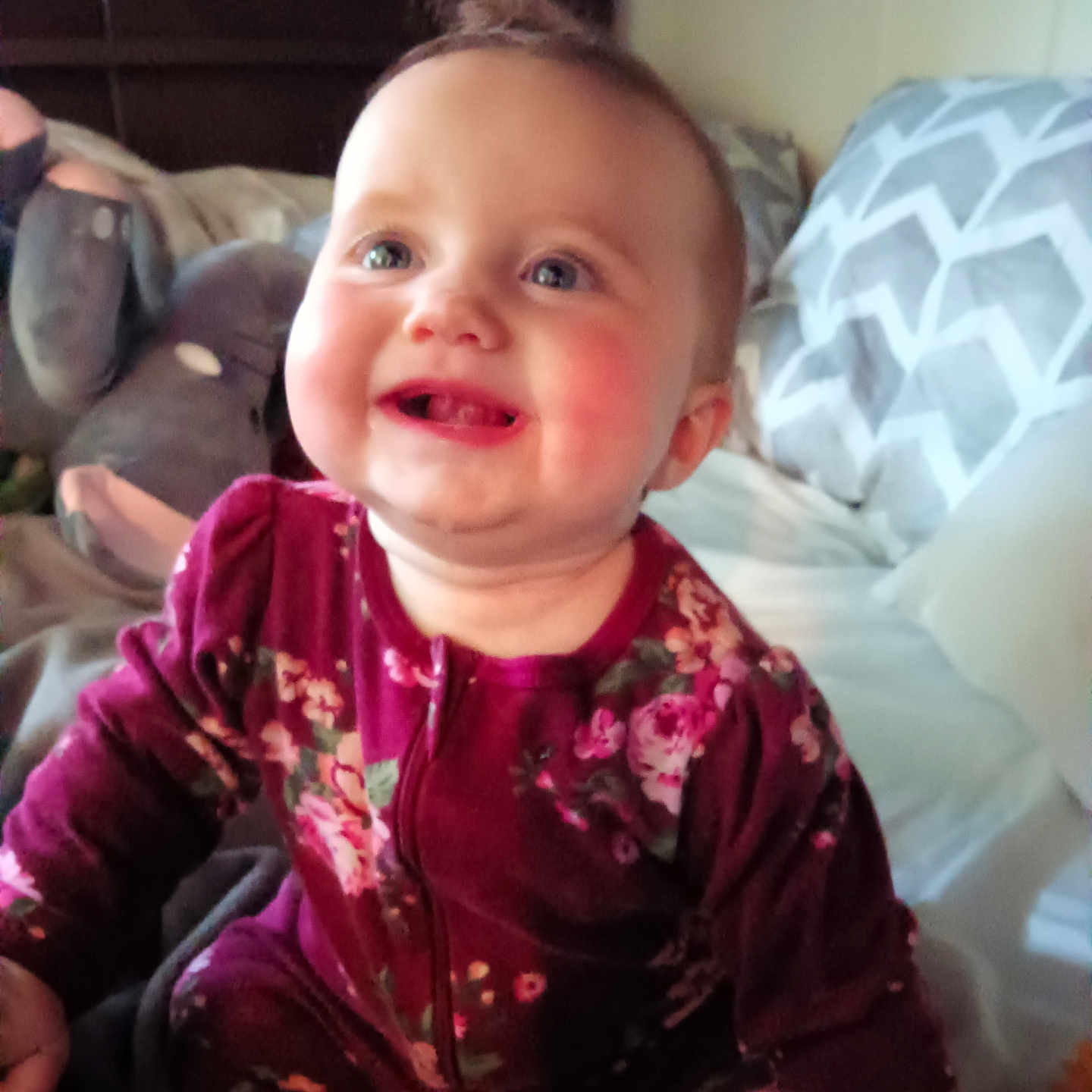 Ava is registered to the contest to win money with this photo: baby, bedroom, blanket, child, cozy, cute, elephant, face, floral_pattern, happy, indoors, infant, pajamas, person, pillow, plush_toy, seated, skin, smiling, young